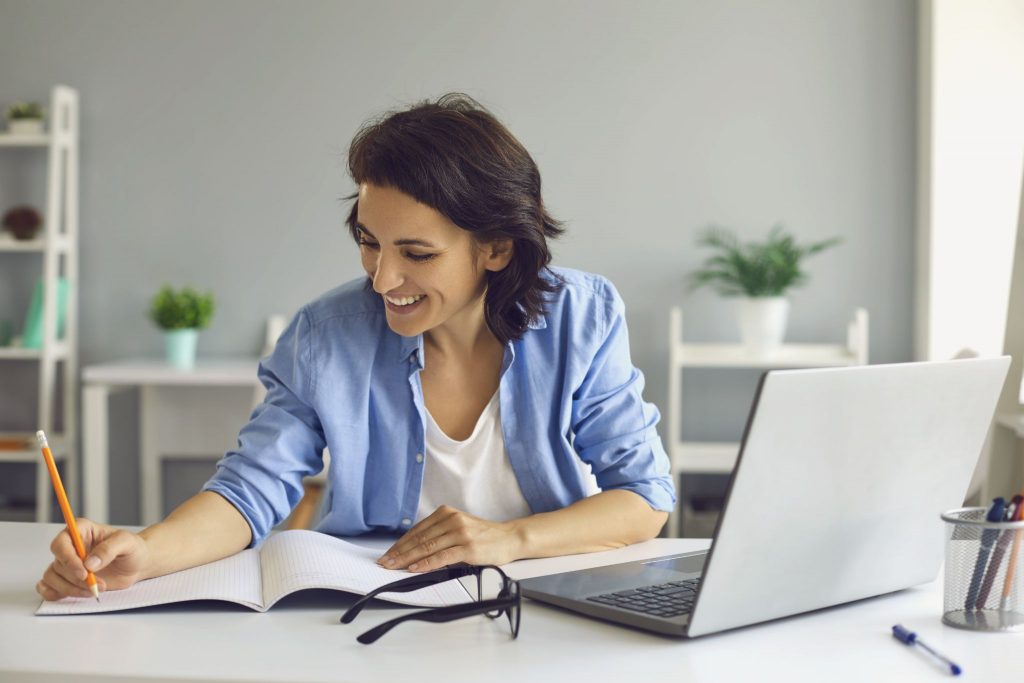 Smiling woman making notes during online meeting on laptop